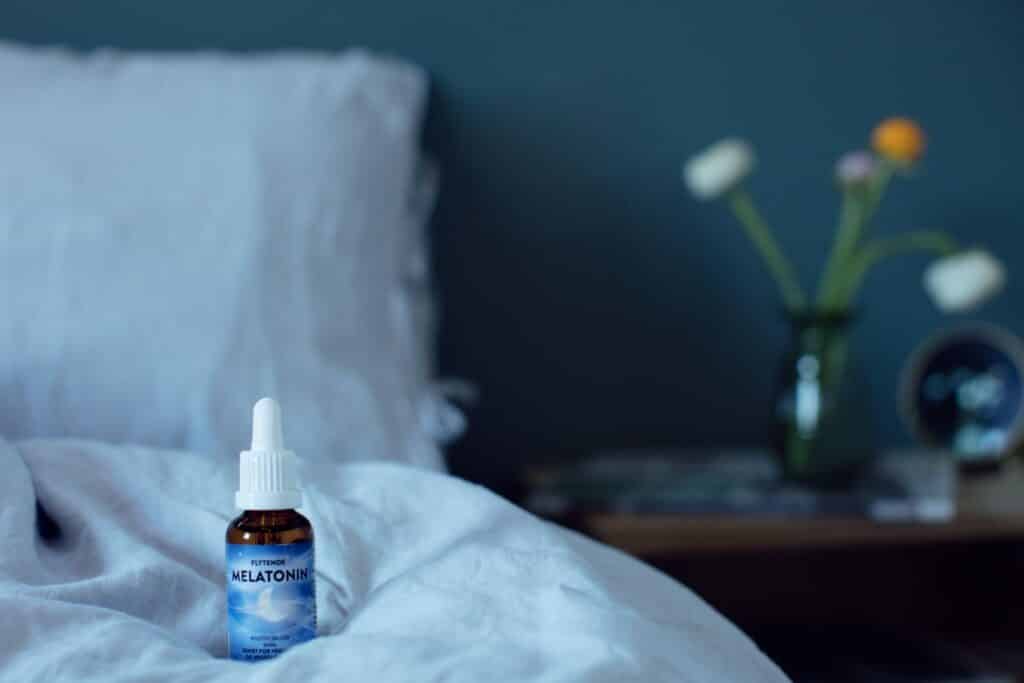 En flaske med flytende melatonin stående på seng